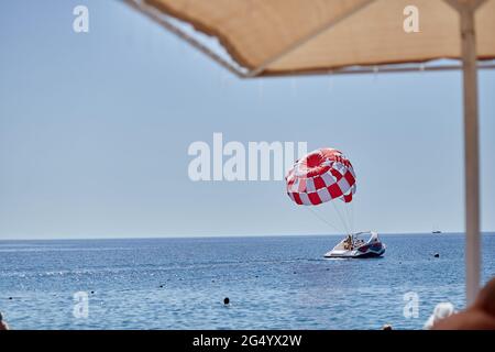 Kemer, Türkei - 25. Mai 2021: Sommeraktivitäten auf dem Wasser: Paragliding mit rotem Fallschirm. Hochwertige Fotos Stockfoto