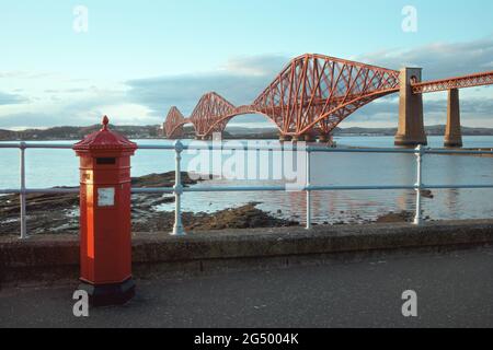 Ein roter britischer Vintage-Briefkasten vor der ikonischen Forth Rail Bridge in South Queensferry, Schottland Stockfoto