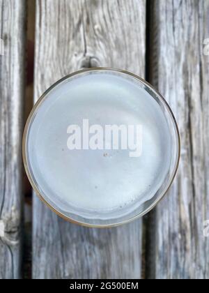 Ein flaches Glas Bier von oben gesehen auf einem Holztisch im Biergarten. Blick auf Schaumschaum. Stockfoto