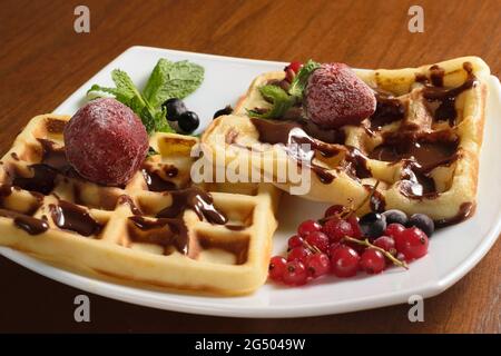 Zwei große Waffeln mit Schokolade, gefrorenen Erdbeeren und Beeren auf einem weißen Teller Stockfoto