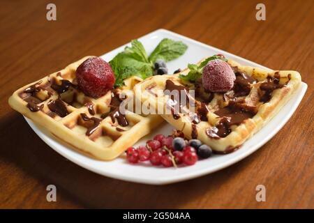 Zwei große Waffeln mit Schokolade, gefrorenen Erdbeeren und Beeren auf einem weißen Teller Stockfoto