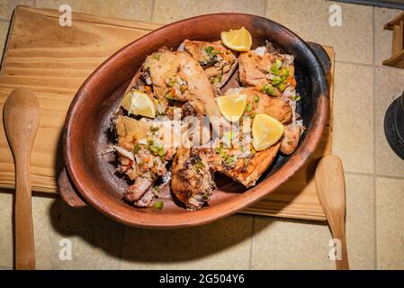 Hausgemachtes gegrilltes Hähnchen mit in Stücke geschnittenen Gewürzen in roter Keramik-Backform auf Holzbrett. Stockfoto