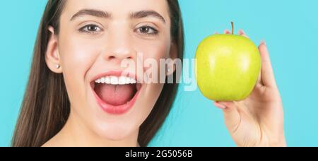 Stomatologie-Konzept. Frau mit perfektem Lächeln hält Apfel, blauer Hintergrund. Frau essen grünen Apfel. Porträt von jungen schönen glücklich lächelnden Frau Stockfoto