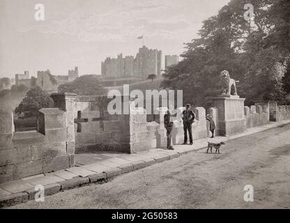 Blick auf das Schloss Alnwick aus dem späten 19. Jahrhundert, eines der Häuser des Herzogs von Northumberland über dem Fluss Aln von der Lion Bridge aus. Benannt nach dem Percy Lion of Cast Lead, der von John Knowles modelliert wurde, wurde die Flussüberquerung von John Adam erbaut und ist ein frühes Beispiel für den neugotischen Stil, Northumberland, England. Stockfoto