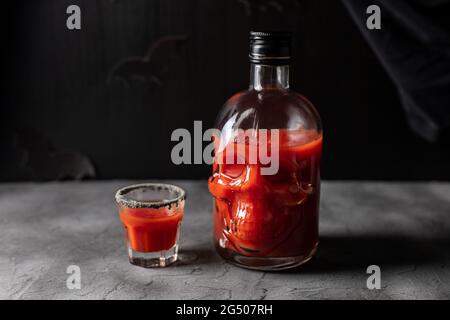 Tomatencocktail in einer kopfförmigen Flasche und Gläsern. Getränk für Halloween-Party auf dunklem Hintergrund Stockfoto