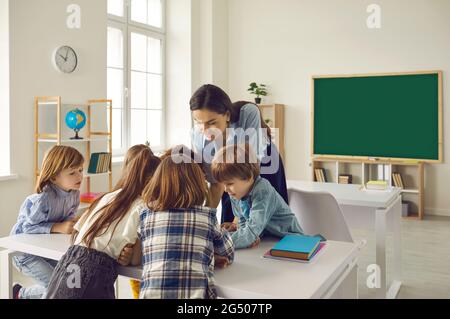 Lehrerin, die Kindern bei ihrer Aufgabe im Klassenzimmer der Grundschule hilft. Stockfoto