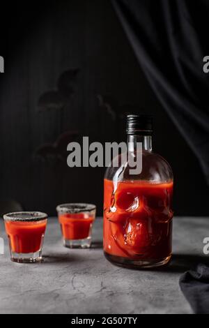 Tomatencocktail in einer kopfförmigen Flasche und Gläsern. Getränk für Halloween-Party auf dunklem Hintergrund Stockfoto