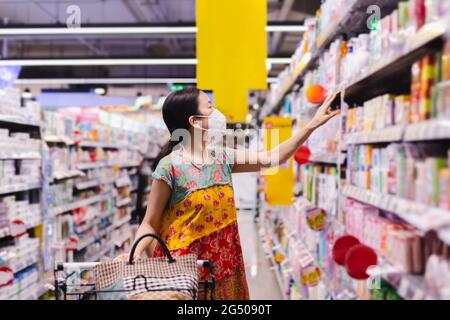 Asiatische Frau in Schutzmaske einkaufen im Supermarkt während covid-19 pardemic. Stockfoto