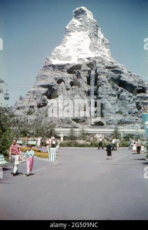 Disneyland, Kalifornien, 1959. Blick auf die Matterhorn Bobbahn, kurz nach dem Bau von der Central Plaza (Hub) aufgenommen und in ihrer ursprünglichen Anordnung dargestellt. Besucher kommen vorbei, ein Wasserfall stürzt die Wand des Berges hinunter und ein Skyway-Auto fährt durch das Zentrum der Attraktion. Stockfoto