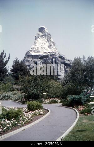 Disneyland, Kalifornien, 1959. Blick auf die Matterhorn Bobbahn kurz nach ihrer Errichtung, aufgenommen aus den angrenzenden Landschaftsgärten. Ein Wasserfall stürzt die Wand des Berges hinunter. Ein Pfad führt durch die wunderschönen Gärten, die mit Blumen, Sträuchern und Bäumen geschmückt sind. Stockfoto