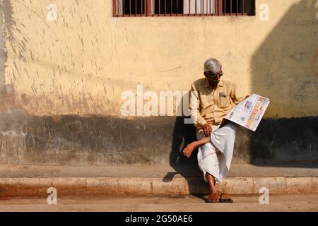 VARANASI, INDIEN - 04. Februar 2021 : Unidentifizierter Mann sitzt bequem und liest indische Zeitung auf der Straße von Varanasi Stockfoto