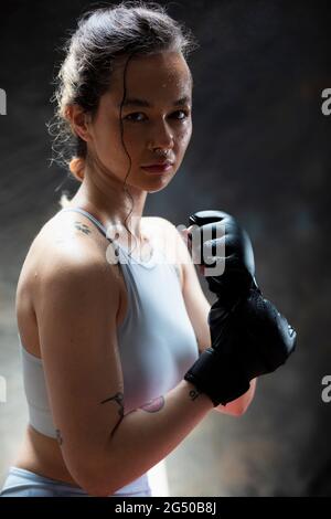 Porträt einer jungen Frau, die Boxhandschuhe trägt und die Kamera anschaut. Sie hat ihre Fäuste auf und ist bereit zu kämpfen. Stockfoto