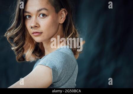 Eine junge, zufriedene, trendige Frau, die für die Kamera posiert. Sie steht vor einem Hintergrund. Stockfoto