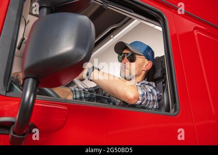 Professioneller kaukasischer Semi-Truck-Fahrer in den 40er Jahren hinter dem Lenkrad seines Tractor Trucks. Schwerlast Cargo Transport Thema. Stockfoto