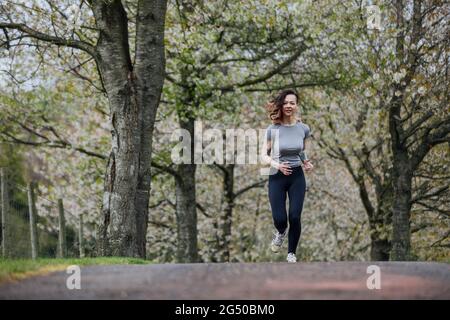 Eine junge Frau, die Gymnastik trägt, joggt im Park unter Blütenbäumen. Stockfoto