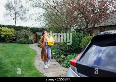 Eine junge Frau, die Lebensmittel in einer wiederverwendbaren Einkaufstasche zu ihrem Auto trägt. Stockfoto