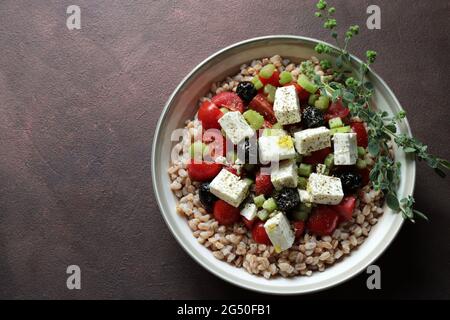 Köstlicher Dinkelsalat mit Feta, Kirschtomaten und Orangano auf braunem Hintergrund. Direkt darüber. Stockfoto