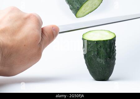 Gurke, die von einem Messer in zwei Hälften geschnitten wird und die andere Hälfte liegt in der Luft Stockfoto