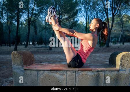 Fitness kaukasische Läuferin, die sich nach dem Lauf in einem Park bei Sonnenuntergang die Beine streckt Stockfoto