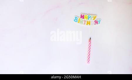 Flaches Lay einer Geburtstagskerze mit einer Papier-Sprechblase auf der Oberseite, geschrieben Happy Birthday in bunten Buchstaben. Mit rosa Marmor Hintergrund. Stockfoto
