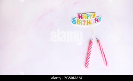Flaches Lay von zwei Geburtstagskerzen mit einer Papier-Sprechblase auf der Oberseite, geschrieben Happy Birthday in bunten Buchstaben. Mit rosa Marmor Hintergrund. Stockfoto