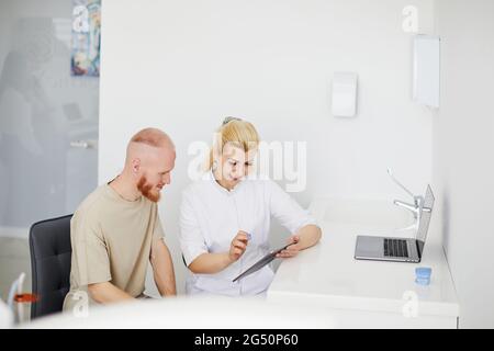 Zahnarzt und Patient wählen die Behandlung in Absprache mit medizinischen Geräten im Hintergrund Stockfoto