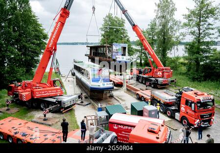 Bad Zwischenahn, Deutschland. Juni 2021. Zwei Mobilkrane heben einen in Längsrichtung geschnittenen Teil des Passagierschiffs „MS Oldenburg“ auf einen Tieflader am Zwischenahner Meer. Das ehemalige Passagierschiff soll per Schwerlastfahrzeug von Bad Zwischenahn aus nach Oldenburg transportiert werden. Dort wird es später als Restaurantschiff im Stadthafen eingesetzt. Quelle: Hauke-Christian Dittrich/dpa/Alamy Live News Stockfoto