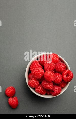 Frische, saftige Himbeeren auf einem kleinen schwarzen Teller. Knallrotes Karmesin aus der Nähe. Sommerliche Beerenpflückzeit. Gesunde Bio-Früchte für Kinder. Vertikal Stockfoto