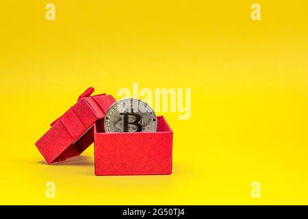 BTC-Geschenk. Bitcoin-Münze in einer Geschenkbox auf gelbem Hintergrund. Postkarte zum Drucken, Banner mit Platz für Text. Stockfoto
