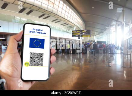 Digitales EU-COVID-Zertifikat mit dem QR-Code auf dem Bildschirm eines Mobiltelefons, das von einer Hand gehalten wird, wobei der Flughafen im Hintergrund unscharf ist. Immunität gegen Covid-19. Stockfoto