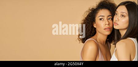 Website-Header von Portrait von zwei wunderschönen gemischten Rennen junge Frauen mit perfekter Haut suchen weg, während posiert isoliert über beige Hintergrund Stockfoto