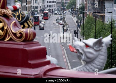 Mit einer flammenden Zunge eines City Griffin im Vordergrund überquert ein Radfahrer den Verkehr und biegt am 24. Juni 2021 in London, England, über die Farringdon Road in der City of London, dem Finanzdistrikt der Hauptstadt, ab. Stockfoto