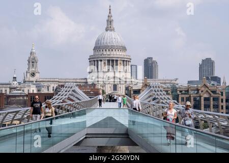 Mit der Kuppel der St. Paul's Cathedral in der Ferne überqueren Fußgänger am 24. Juni 2021 in London, England, die Themse auf der Millennium Bridge. Londons neueste Flussüberquerung seit über 100 Jahren fiel mit dem Millennium zusammen. Sie wurde am 10. Juni 2000 in aller Eile fertiggestellt und für die Öffentlichkeit zugänglich gemacht, als schätzungsweise 100,000 Menschen sie überquerten, um zu entdecken, dass die Struktur so stark oszillierte, dass sie 2 Tage später geschlossen werden musste. In den nächsten 18 Monaten fügten Designer Dämpfer hinzu, um das Wackeln zu stoppen, aber es symbolisierte bereits das, was peinlich war und im britischen Stolz versagte. Nun der britische Stan Stockfoto