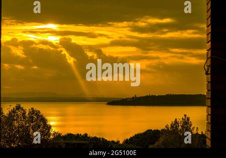 Goldener Sonnenuntergang mit Sonnenstrahl über dem Trasimeno-See und der Isola Maggiore (Großinsel) in Umbrien Stockfoto