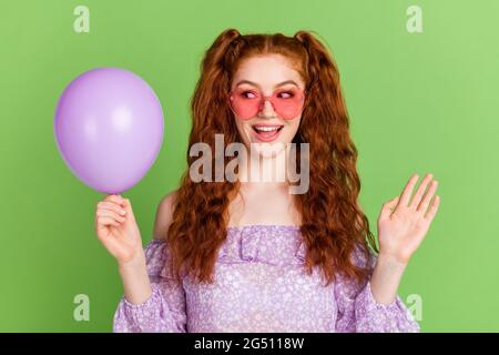 Foto von beeindruckt roten Frisur junge Dame halten Ballon tragen violette Bluse Brille isoliert auf grünem Hintergrund Stockfoto