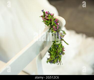 Blumenhochzeit Kopfstück drapiert über einem weißen Stuhl mit dem Hochzeitskleid im Hintergrund. Stockfoto