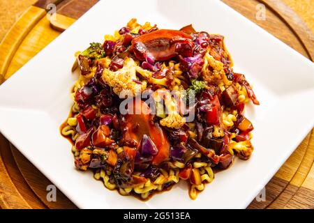 Ein quadratischer weißer Teller mit vegetarischer Yakissoba auf einem Tisch. Stockfoto