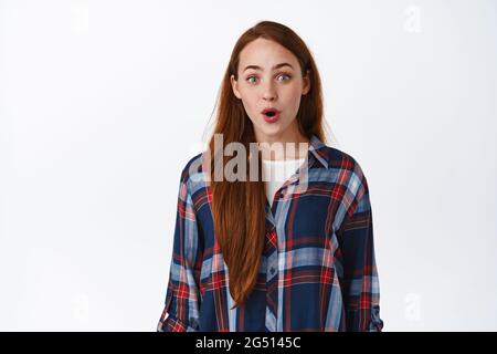 Wow, super cool. Beeindrucktes Teenager-Rotschopf-Mädchen, keuchen und starren vor der Kamera, schauend mit Aufregung auf ehrfürchtige Promo im Laden, stehend über Stockfoto