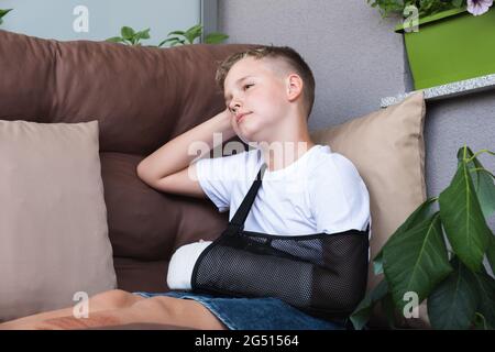 Trauriges Kind mit gebrochenem Arm in häuslichen Umgebung. Auf die Hand eines kleinen Jungen gegossen. Stockfoto