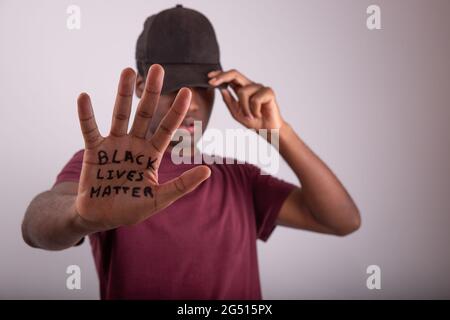 Nahaufnahme der Hand eines afrikanischen Mannes mit dem Zitat „Black Lives Matter“. Mann, der eine Mütze trägt, die seine Augen bedeckt. Verschwommener Hintergrund und Gesicht und Handfläche Stockfoto