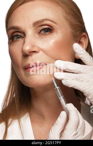 Porträt einer schönen älteren Frau in einem weißen Hemd mit klassischem Make-up und blondem Haar mit Spritze in den Händen Stockfoto