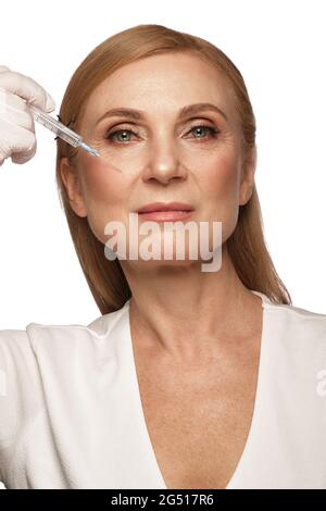 Porträt einer schönen älteren Frau in einem weißen Hemd mit klassischem Make-up und blondem Haar mit Spritze in den Händen Stockfoto