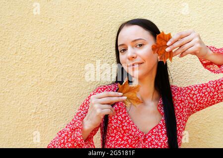 Schöne glückliche junge Frau hält Herbstblätter. Mädchen im Freien in rotem Kleid Stockfoto