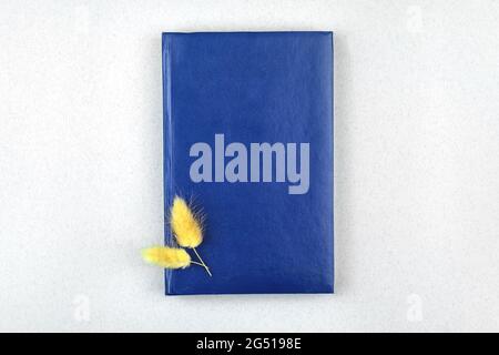 Minimaler Arbeitsplatzaufbau mit blauem Ledernotepad und getrockneten Blumen, Office-Desktop von oben Stockfoto