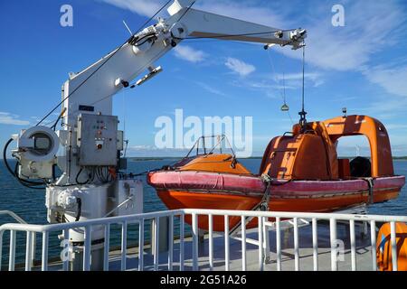 Orange Rettungsboot, Rettungsboot der Fähre segelt auf dem Meer mit blauem Himmel und Küste im Hintergrund. Stockfoto