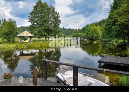 Kleines Boot schwimmt auf einem kleinen See, ordentlich zu hölzernen Steg, Brücke und Wald im Hintergrund Stockfoto