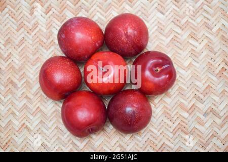 Rohe Bio-rote Pflaumen auf weißem Hintergrund, rote kastanienbraune Nuancen, frische glänzende Früchte. Farm frische Bio-roten Pflaumen produzieren geerntet. Auf Jute Art gewebt b Stockfoto