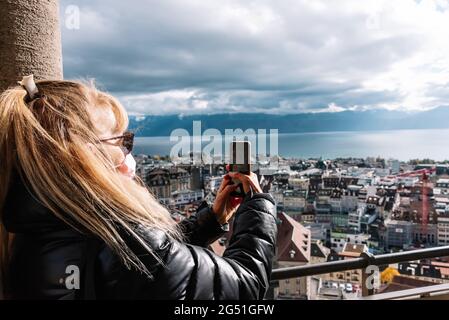 Unerkannte blonde Frau mit Gesichtsmaske, die ein Foto einer urbanen Landschaft gemacht hat. Stockfoto