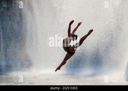 Silhouette einer Frau, die akrobatische Sprünge gegen den Brunnen macht Stockfoto