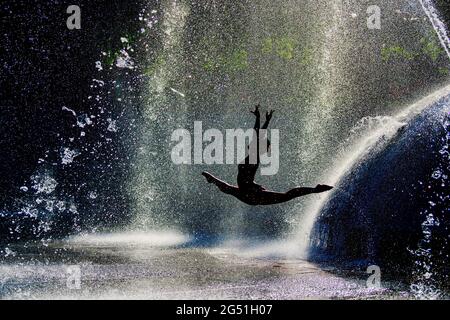 Silhouette einer Frau, die akrobatische Sprünge gegen den Brunnen macht Stockfoto